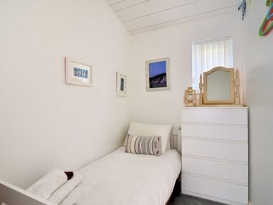 A small bedroom with a single bed a white chest of drawers and framed pictures on the wall at The Beach Hut in Lyme Regis