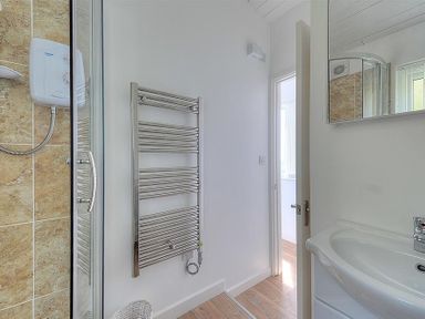 A bathroom with a shower, towel rack, sink, mirror, and a door leading to another room at The Beach Hut in Lyme Regis