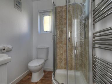 A bathroom with a toilet a corner shower with glass doors and a chrome towel radiator at The Beach Hut in Lyme Regis