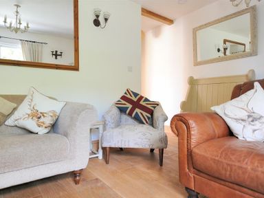 A living room with a beige sofa a patterned armchair with a union jack cushion and a brown leather sofa with animal print cushions at Bethel Cottage in Lyme Regis