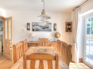 A dining room with a wooden table and chairs a sideboard with a lamp and globe wall lights and curtains at Bethel Cottage in Lyme Regis