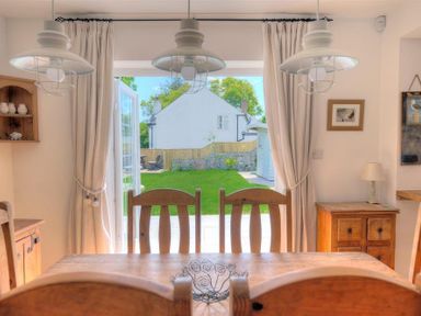 A dining room with wooden chairs and table opening to a garden at Bethel Cottage Lyme Regis