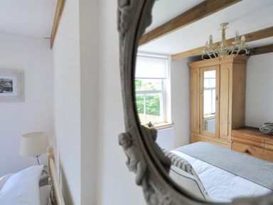 A bedroom with a bed a wooden wardrobe a dresser a window and a chandelier at Bethel Cottage Lyme Regis
