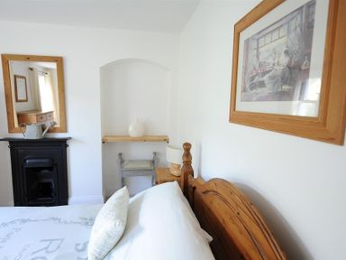 A bedroom with a wooden bed frame a mirror over a black fireplace a wooden side table with a lamp and framed artwork on the wall at Bethel Cottage in Lyme Regis
