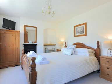 A bedroom with a wooden bed and white bedding two bedside tables with lamps a wardrobe a television and a mirror at Bethel Cottage in Lyme Regis