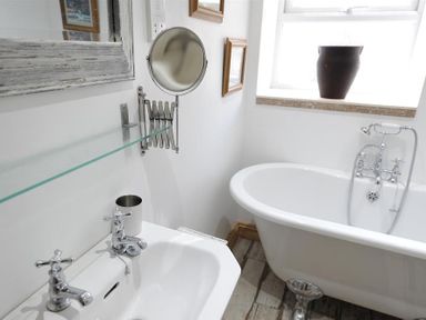 A bathroom with a sink, a freestanding bathtub, a wall-mounted glass shelf, and a window with a brown vase at Bethel Cottage in Lyme Regis