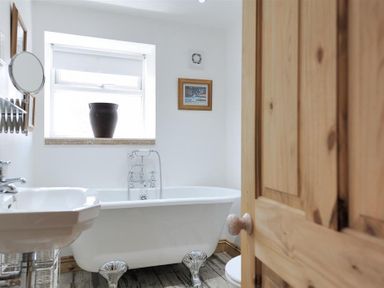 A bathroom with a clawfoot bathtub a sink with a tap a window with a vase and a wooden door at Bethel Cottage in Lyme Regis