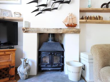 A wood burning stove with a wooden mantel and decorative ship and bucket in a living room at Bethel Cottage Lyme Regis