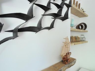 A metal wall sculpture of birds above a wooden model ship and wooden shelves with decorative items at Bethel Cottage in Lyme Regis