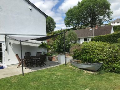 A backyard patio with a table and chairs under a canopy next to a boat planter and bushes at Bethel Cottage in Lyme Regis