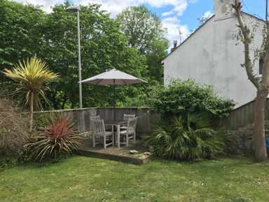 A garden with a wooden table and chairs under a patio umbrella surrounded by plants and a wooden fence at Bethel Cottage in Lyme Regis