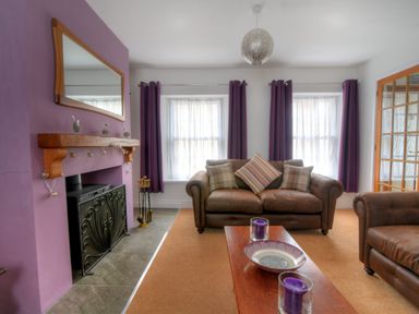 A living room with leather sofas a wooden coffee table with candles a fireplace with a mirror above and purple curtains at Sunnyside in Colyton