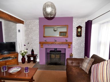 A living room with a purple accent wall a wood-burning stove a brown sofa and a wooden coffee table at Sunnyside Colyton