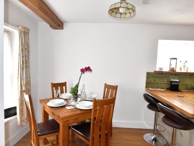 A dining area with a wooden table set for four next to a kitchen counter with two bar stools at Sunnyside in Colyton