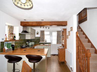 A kitchen with wooden countertops two bar stools wooden stairs and a wooden cabinet at Sunnyside in Colyton