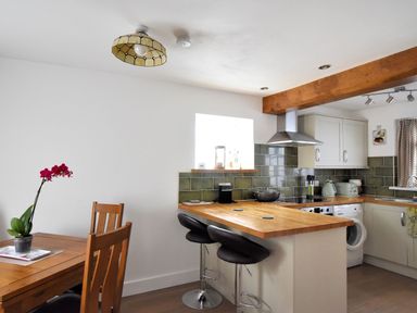A kitchen with wooden countertops green tiled backsplash bar stools and a dining table with chairs at Sunnyside in Colyton