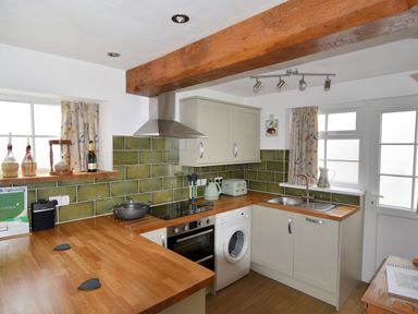 A kitchen with wooden countertops green tiled backsplash a stove sink washing machine and windows at Sunnyside in Colyton