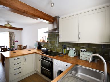 A kitchen with wooden countertops green tiled backsplash a stove sink and dining table at Sunnyside in Colyton