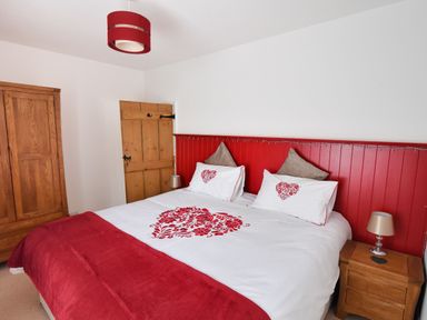 A bedroom with a double bed featuring red and white bedding with heart designs wooden furniture and a red lampshade at Sunnyside in Colyton