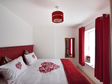 A bedroom with a bed with white and red bedding next to a window with red curtains at Sunnyside in Colyton