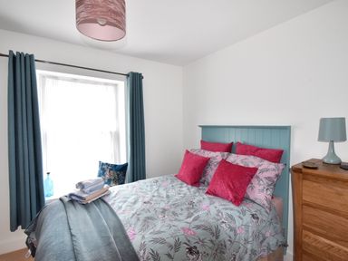 A bedroom with a bed with floral bedding and pink pillows a wooden dresser and blue curtains at Sunnyside in Colyton