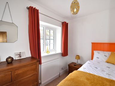 A bedroom with an orange headboard, mustard yellow bedding, wooden dresser, bedside table with lamp, and orange curtains at Sunnyside in Colyton