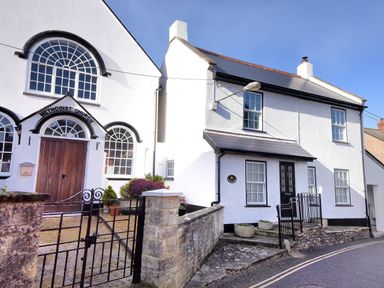 A white Methodist church building and adjacent white house with black trim on a street at Sunnyside in Colyton