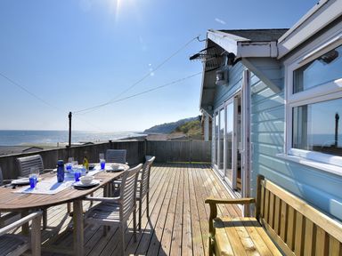 An outdoor wooden deck with a dining table set with dishes and glasses overlooking the sea at Ammonite in Lyme Regis