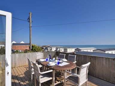 A wooden deck with a dining table and six chairs set for a meal with the ocean and houses in the background at Ammonite in Lyme Regis