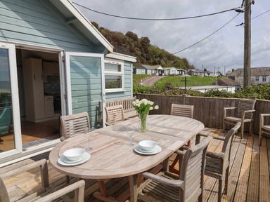 An outdoor wooden deck with a dining table and chairs set with bowls glasses and flowers at Ammonite Lyme Regis
