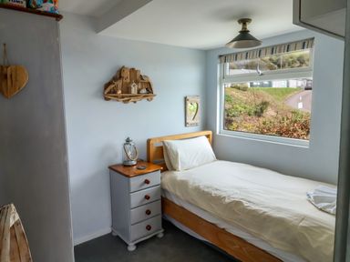 A small bedroom with a single bed next to a window and a bedside table with a lantern at Ammonite in Lyme Regis