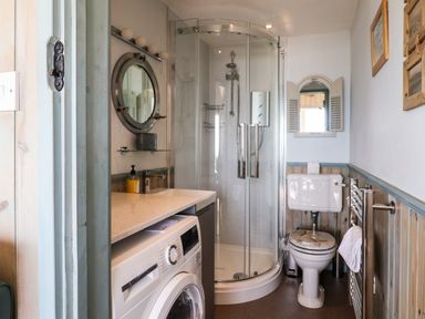 A bathroom with a shower, toilet, washing machine, sink, and mirror at Ammonite in Lyme Regis