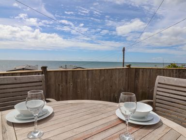 A wooden outdoor table set for two with wine glasses and plates on a balcony overlooking the sea at Ammonite in Lyme Regis