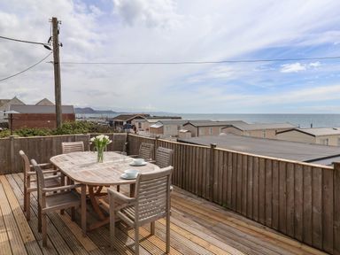An outdoor deck with a wooden table and chairs overlooking the sea and nearby buildings at Ammonite in Lyme Regis