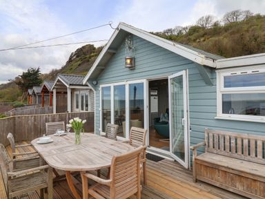 A wooden deck with a table and chairs outside beach huts on a hillside at Ammonite in Lyme Regis