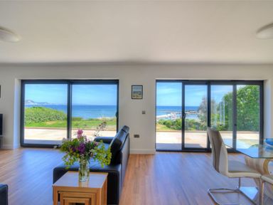 A living room with glass doors overlooking the sea and a table with flowers at Harbour Heights Cottage Lyme Regis