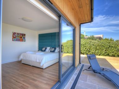 A bedroom with a double bed and towels on it next to a sliding glass door opening to an outdoor patio with a blue lounge chair at Harbour Heights Cottage in Lyme Regis
