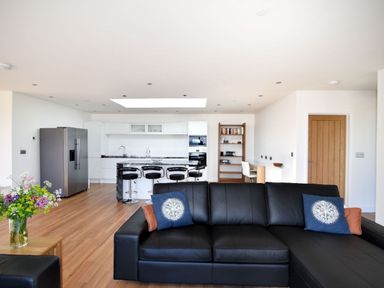 A living room with a black leather sofa and a kitchen with a refrigerator and bar stools at Harbour Heights Cottage in Lyme Regis