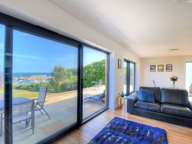 A living room with a black leather sofa blue rug and large sliding glass doors overlooking a patio and garden at Harbour Heights Cottage in Lyme Regis
