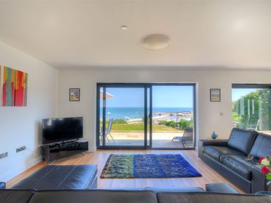 A living room with black leather sofas a television and a sliding glass door with a view of the sea at Harbour Heights Cottage Lyme Regis