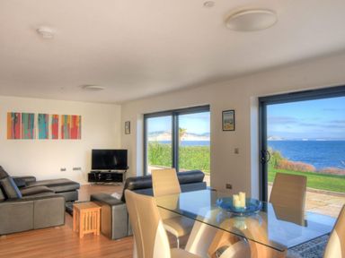 A living room and dining area with leather sofas glass dining table and large windows showing a sea view at Harbour Heights Cottage Lyme Regis