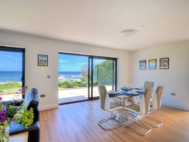 A dining area with glass table and four chairs near large windows overlooking the sea at Harbour Heights Cottage in Lyme Regis