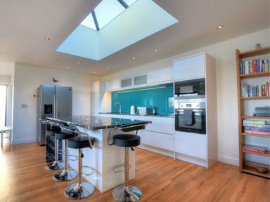 A kitchen with a marble island and black bar stools with a skylight and wooden floor at Harbour Heights Cottage in Lyme Regis