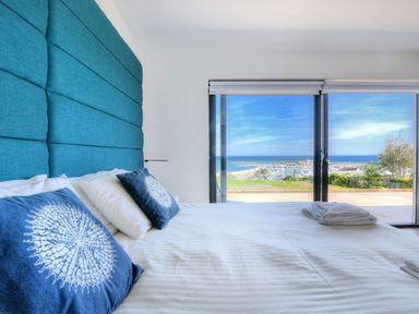 A bedroom with a large bed and blue pillows facing a glass door with a view of the ocean at Harbour Heights Cottage Lyme Regis