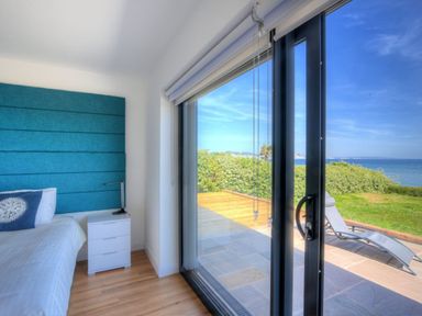 A bedroom with a bed and blue headboard next to a sliding glass door opening to a patio and sea view at Harbour Heights Cottage Lyme Regis