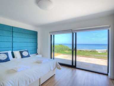 A bedroom with a large bed and a blue padded headboard with a view of the sea through sliding glass doors at Harbour Heights Cottage in Lyme Regis