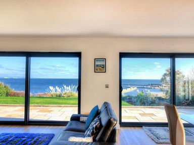 A living room with a black leather sofa and sliding glass doors showing a sea view at Harbour Heights Cottage in Lyme Regis