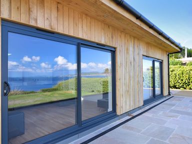 A wooden building with large glass sliding doors reflecting the sea and sky at Harbour Heights Cottage in Lyme Regis