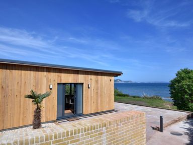 A wooden building with glass doors near a brick wall overlooking the sea at Harbour Heights Cottage in Lyme Regis