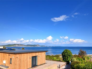 A wooden building with double doors near a coast with sea and hills at Harbour Heights Cottage Lyme Regis
